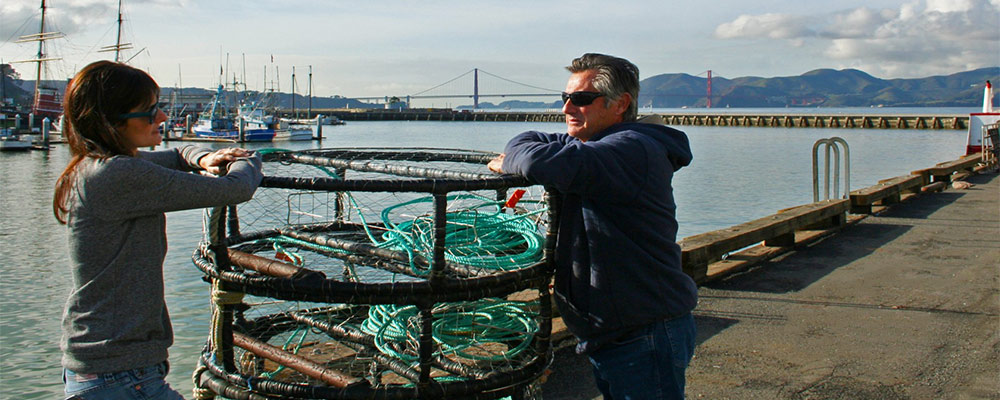 photo of two people talking while leaning up against crab traps, with the golden gate bridge in the background