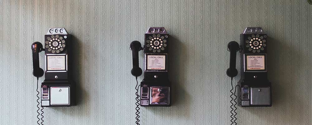 photo of three black and silver rotary phones on a green colored wall