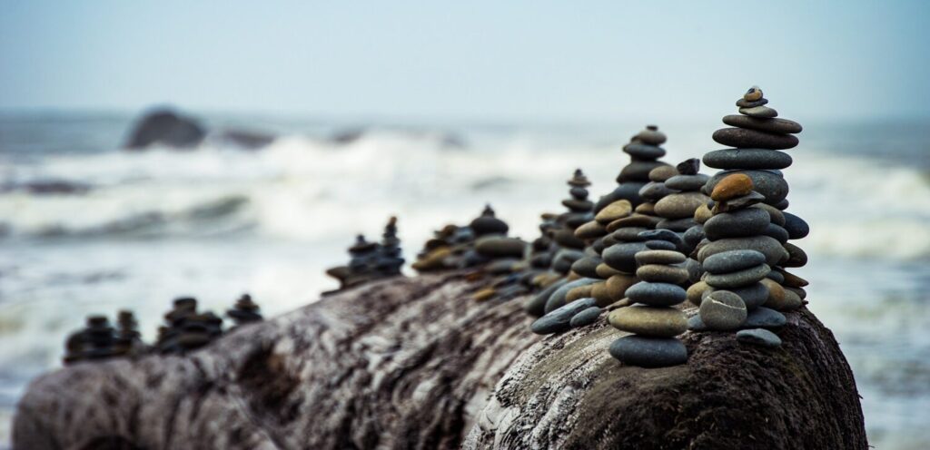 Photo of a log on the beach with small groups of rock piled on it.