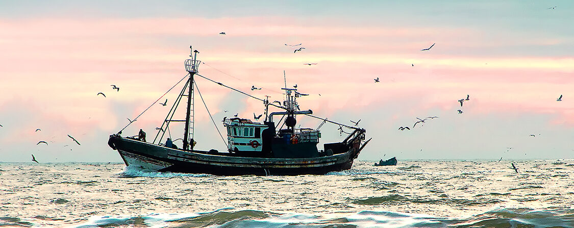 Photo of a fishing boat in the water during a pink and purple sunset