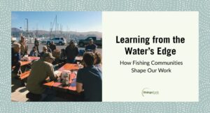 Group meeting near water with fishing boats behind them