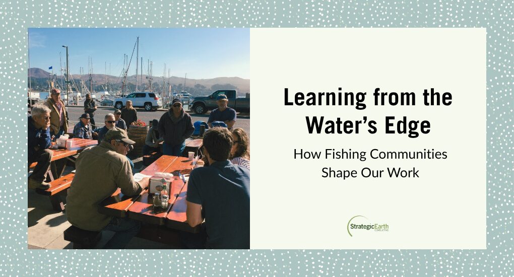 Group meeting near water with fishing boats behind them